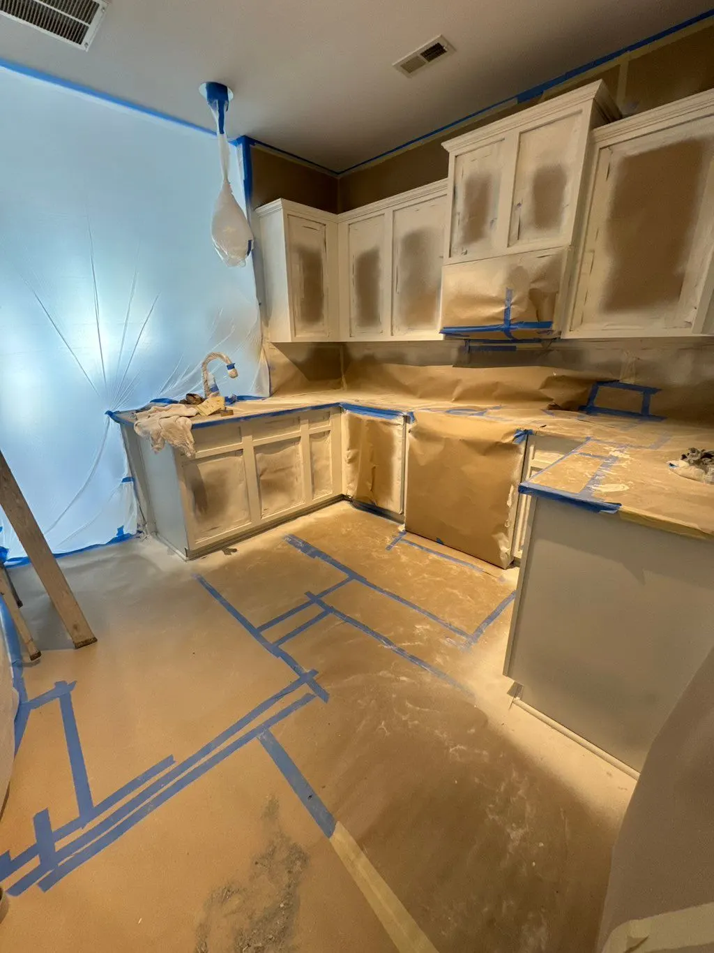 Kitchen cabinets masked and prepped with floors covered, mid-job