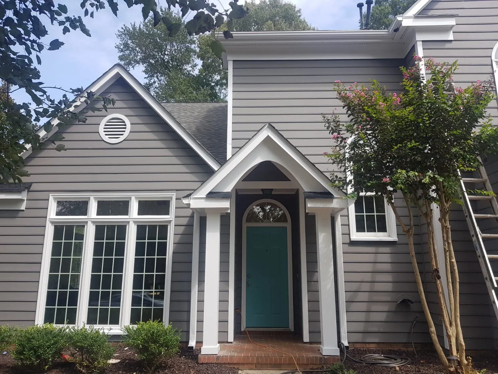 Gray two-story house with white trim, a teal front door and arched windows