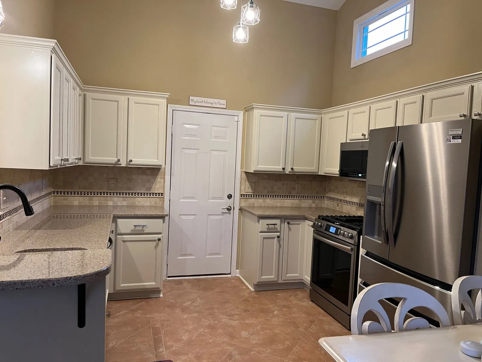 Kitchen with cream cabinets under a tall ceiling and a high window