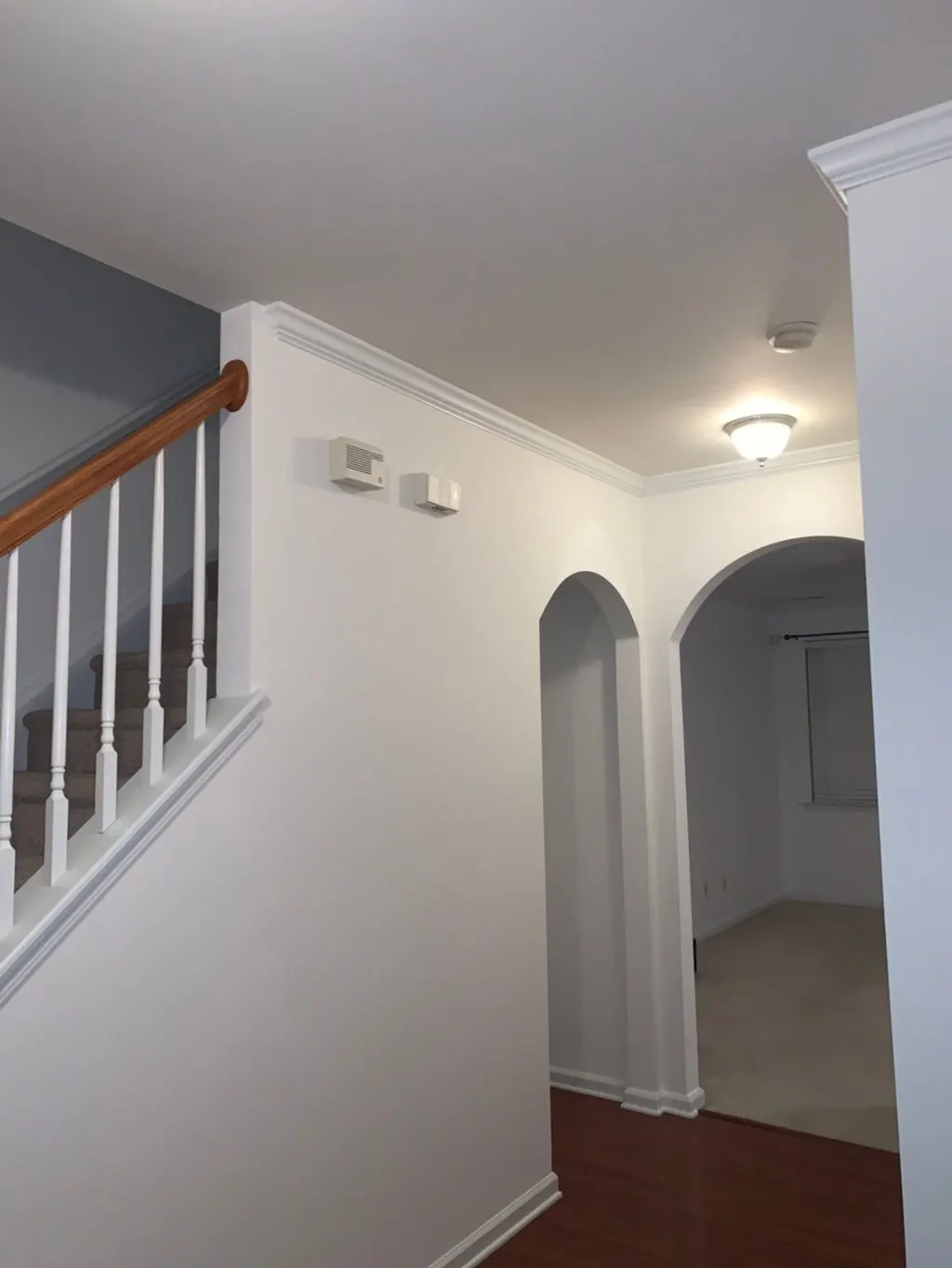 Hallway with a white stair rail, crown moulding and arched doorway