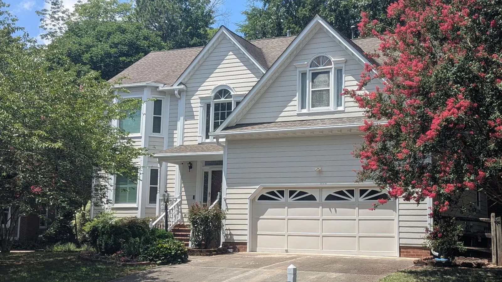 White two-story house with a covered porch and a pink crepe myrtle